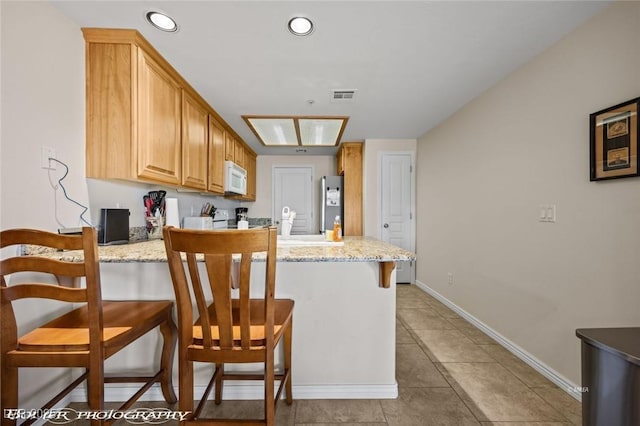 kitchen with light brown cabinets, stainless steel refrigerator, a kitchen breakfast bar, kitchen peninsula, and light stone countertops