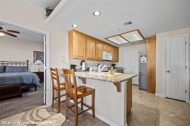 kitchen featuring electric stove, a breakfast bar, ceiling fan, light stone countertops, and kitchen peninsula