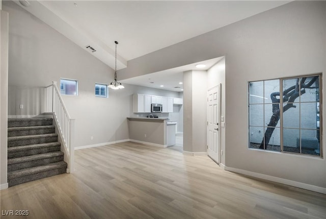 unfurnished living room with an inviting chandelier, high vaulted ceiling, and light hardwood / wood-style flooring