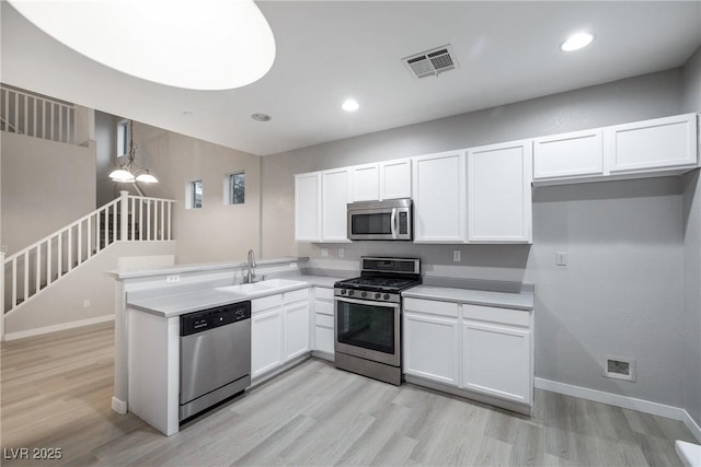 kitchen featuring appliances with stainless steel finishes, decorative light fixtures, sink, white cabinets, and kitchen peninsula