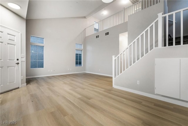 unfurnished living room with beam ceiling, a towering ceiling, and light hardwood / wood-style floors