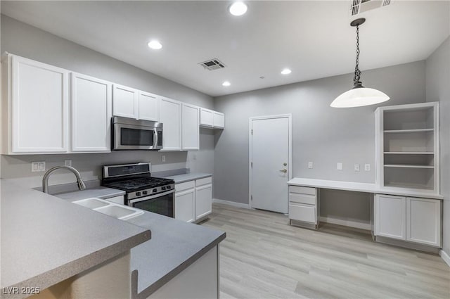 kitchen with pendant lighting, sink, white cabinets, stainless steel appliances, and light wood-type flooring