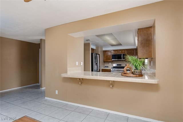 kitchen featuring appliances with stainless steel finishes, light tile patterned floors, a kitchen bar, and kitchen peninsula