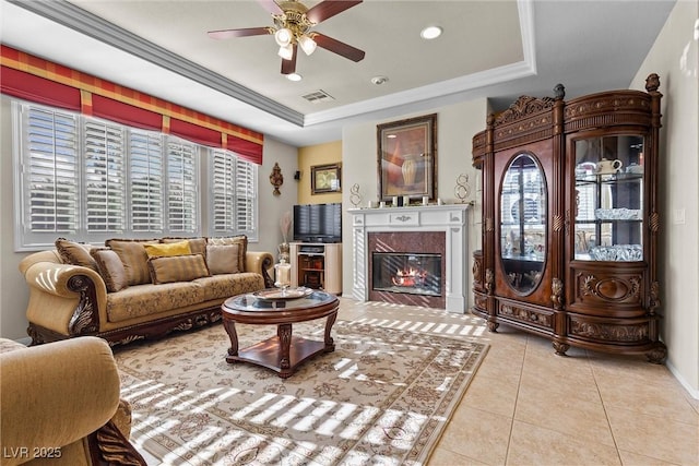 tiled living room with a tray ceiling, a fireplace, ornamental molding, and ceiling fan