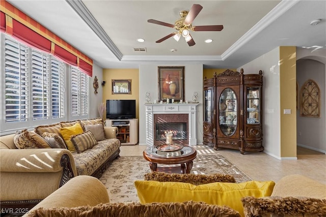 living room with light tile patterned flooring, a premium fireplace, a raised ceiling, and crown molding