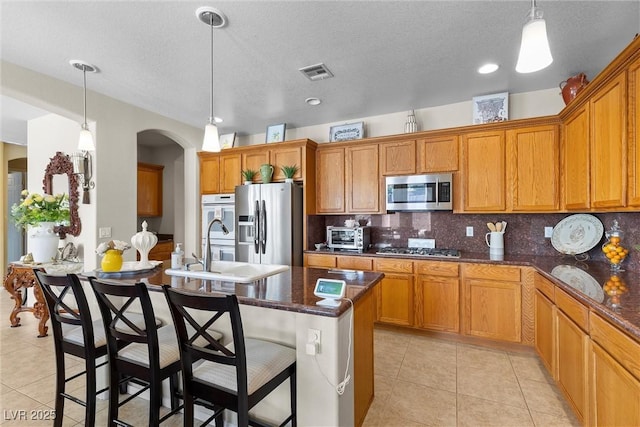 kitchen with appliances with stainless steel finishes, decorative light fixtures, sink, dark stone counters, and light tile patterned floors