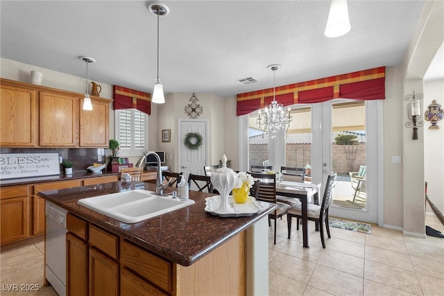 kitchen featuring sink, light tile patterned floors, dark stone countertops, white dishwasher, and a center island with sink