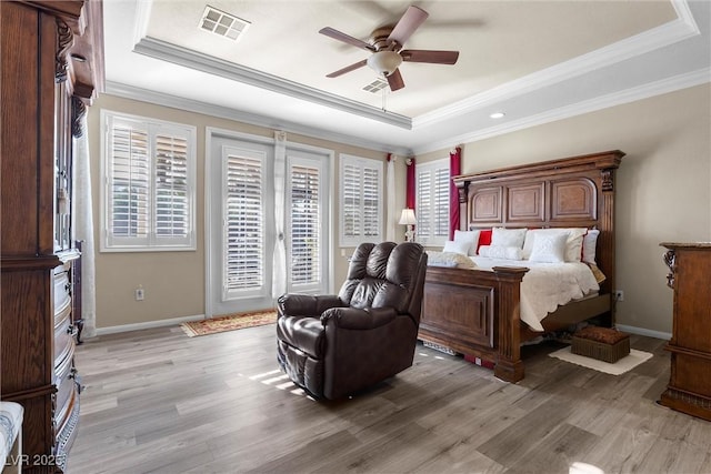 bedroom featuring access to exterior, light hardwood / wood-style floors, and a tray ceiling