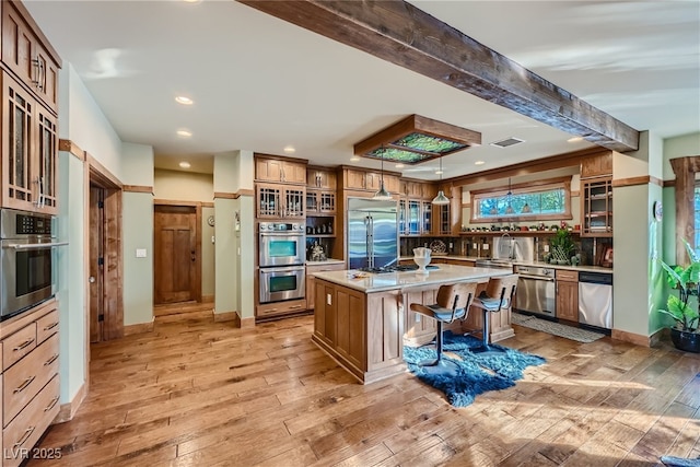 kitchen with light hardwood / wood-style flooring, appliances with stainless steel finishes, a kitchen breakfast bar, pendant lighting, and a kitchen island with sink