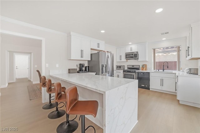 kitchen with sink, a breakfast bar, white cabinetry, stainless steel appliances, and light stone counters