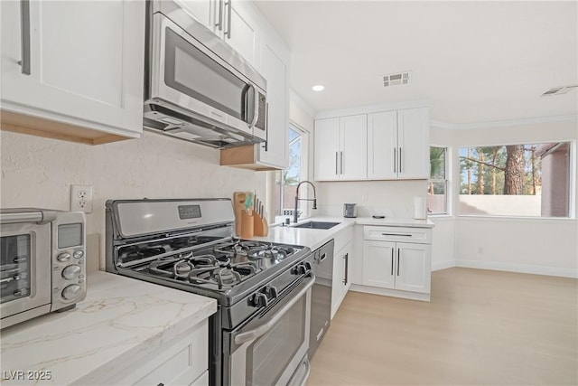 kitchen with sink, crown molding, appliances with stainless steel finishes, light stone counters, and white cabinets