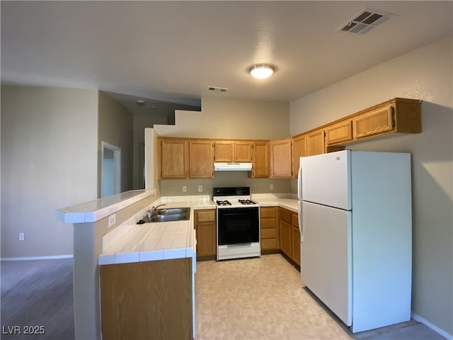 kitchen with gas stove, tile counters, freestanding refrigerator, under cabinet range hood, and visible vents