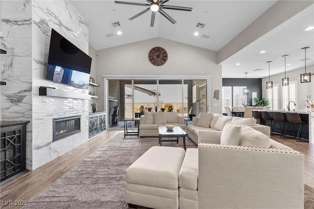 living area featuring visible vents, a ceiling fan, a premium fireplace, wood finished floors, and vaulted ceiling