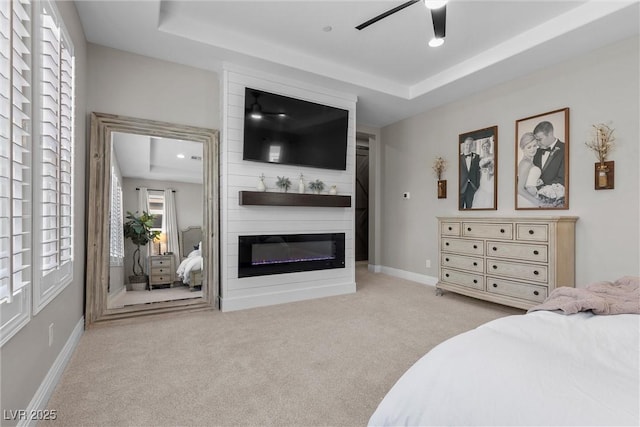 carpeted bedroom featuring ceiling fan, a fireplace, baseboards, and a raised ceiling