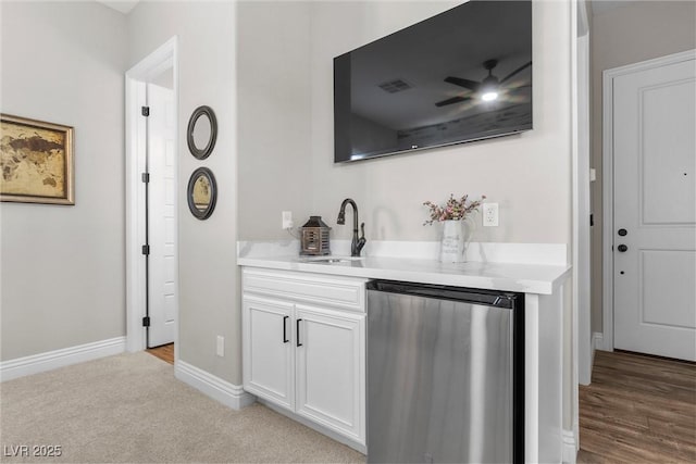 bar with light carpet, a sink, ceiling fan, dishwasher, and baseboards