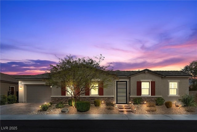 single story home featuring driveway, stone siding, an attached garage, and stucco siding