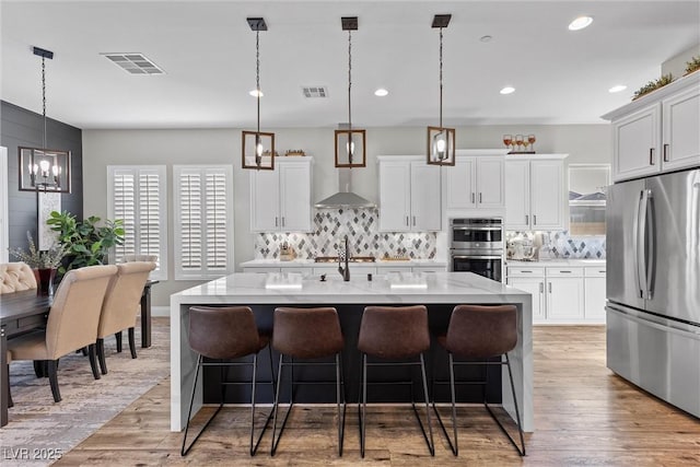 kitchen featuring stainless steel appliances, visible vents, light wood finished floors, and wall chimney exhaust hood