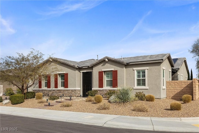 single story home with stone siding, a tile roof, fence, and stucco siding