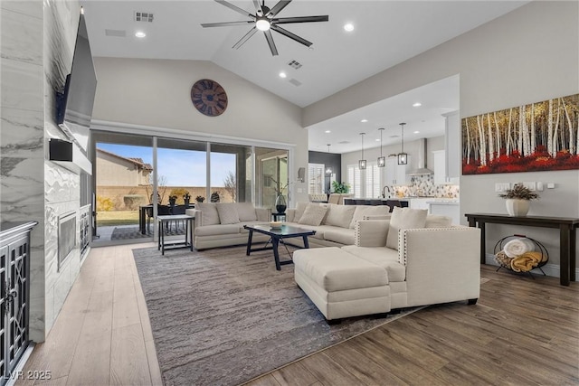 living room featuring a ceiling fan, visible vents, a fireplace, and wood finished floors