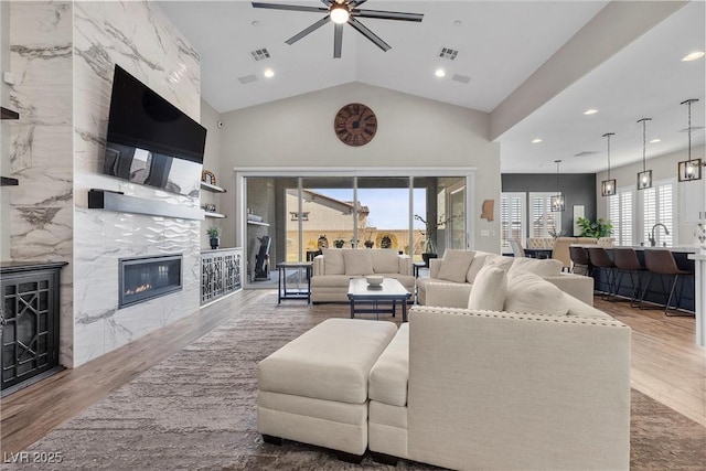 living room featuring visible vents, ceiling fan, wood finished floors, vaulted ceiling, and a fireplace