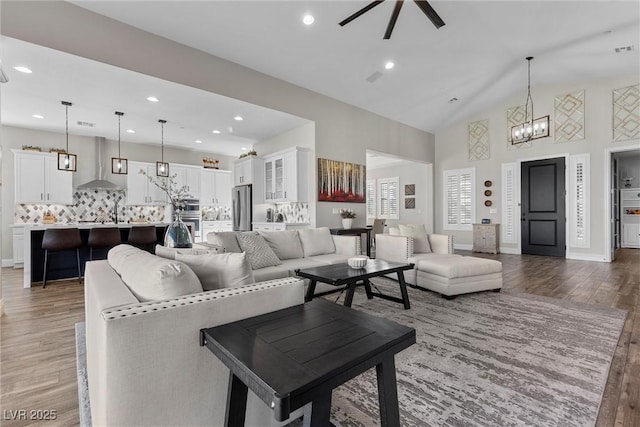 living room featuring high vaulted ceiling, recessed lighting, ceiling fan with notable chandelier, baseboards, and light wood-type flooring