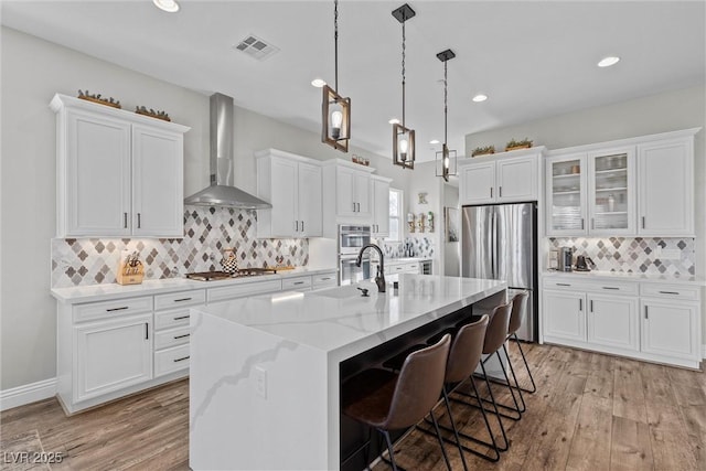 kitchen featuring white cabinets, wall chimney exhaust hood, visible vents, and stainless steel appliances