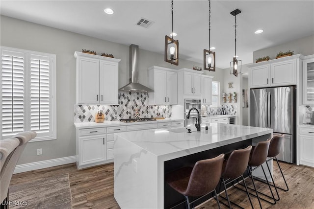 kitchen with tasteful backsplash, visible vents, wall chimney exhaust hood, appliances with stainless steel finishes, and wood finished floors