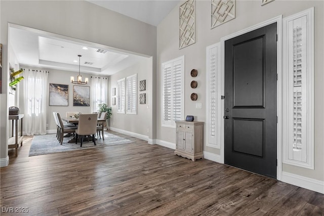 foyer entrance featuring baseboards, a chandelier, a raised ceiling, and dark wood finished floors