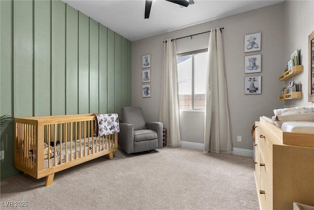 bedroom with a crib, ceiling fan, baseboards, and carpet flooring