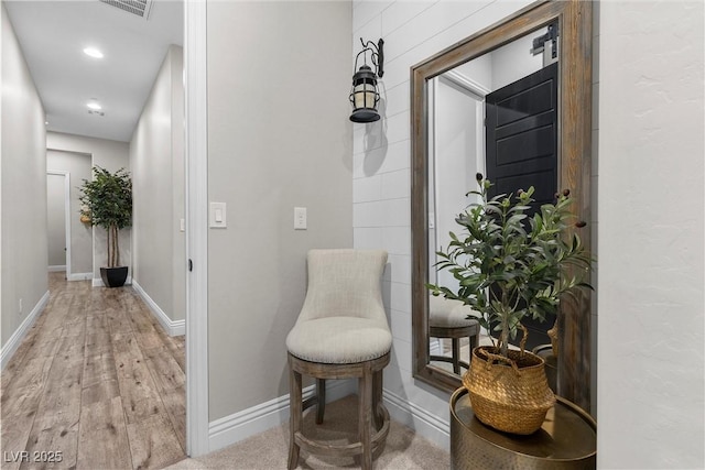 hall with light wood-type flooring, visible vents, and baseboards