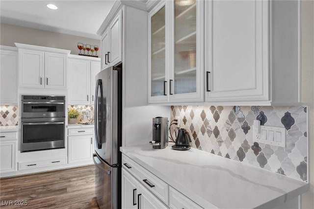 kitchen featuring dark wood finished floors, appliances with stainless steel finishes, light stone counters, white cabinetry, and backsplash