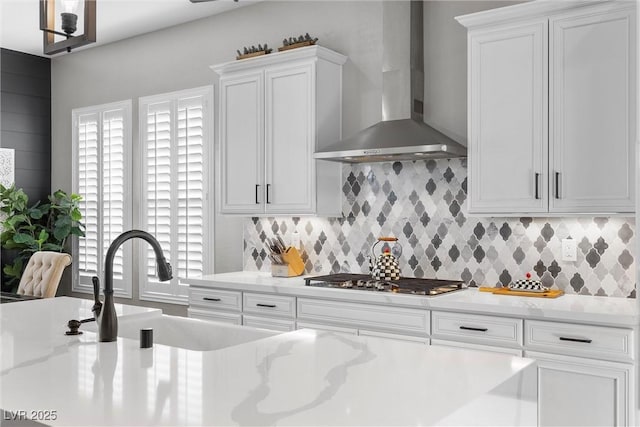 kitchen with stainless steel gas cooktop, light countertops, wall chimney range hood, and white cabinetry