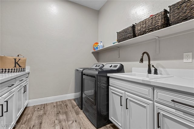 clothes washing area with cabinet space, light wood-style flooring, washing machine and dryer, a sink, and baseboards