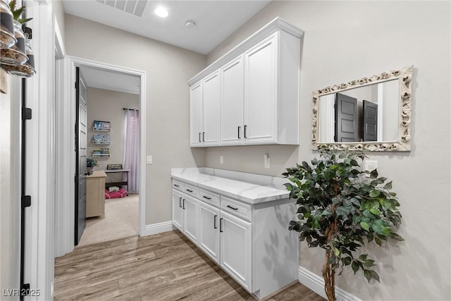 kitchen with light wood finished floors, visible vents, baseboards, light stone countertops, and white cabinetry