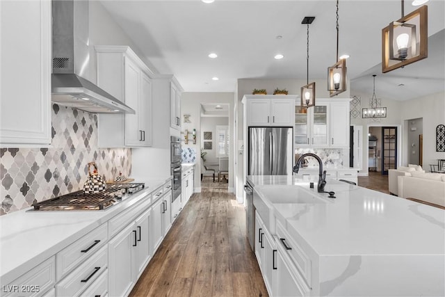 kitchen with wall chimney exhaust hood, stainless steel appliances, a large island with sink, white cabinetry, and a sink