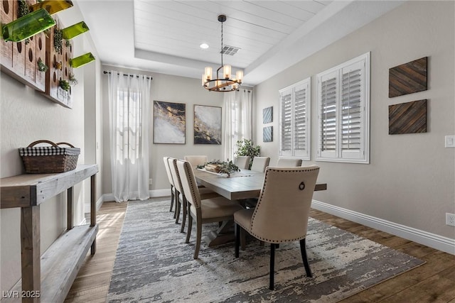 dining space featuring a tray ceiling, wood finished floors, visible vents, and baseboards