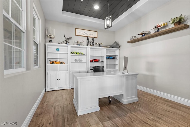 unfurnished office featuring a tray ceiling, wood finished floors, wood ceiling, and baseboards