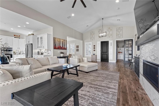 living room with high vaulted ceiling, dark wood-style flooring, a glass covered fireplace, and recessed lighting