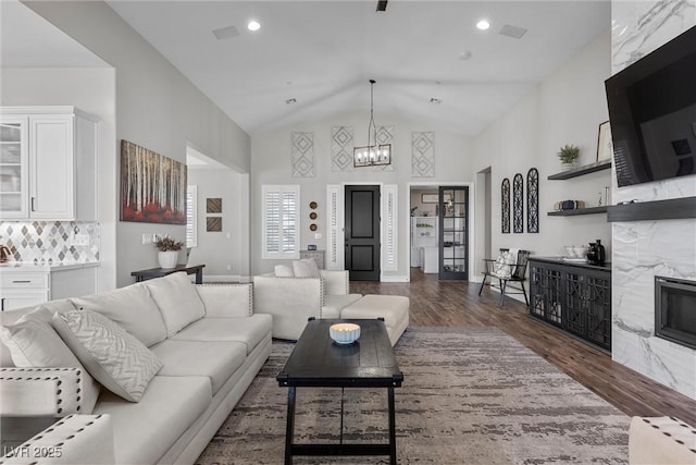 living area with dark wood finished floors, recessed lighting, a chandelier, a high end fireplace, and high vaulted ceiling