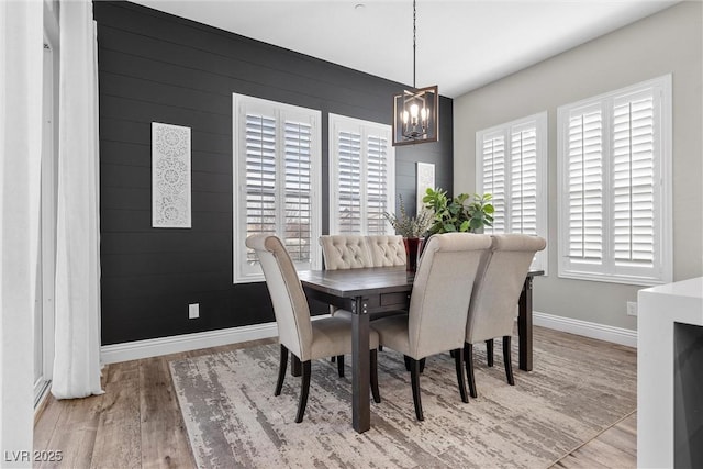 dining area featuring an inviting chandelier, wood walls, baseboards, and wood finished floors