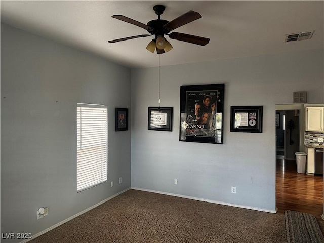 empty room with ceiling fan and dark colored carpet