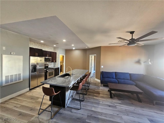 kitchen with a kitchen bar, sink, a center island with sink, light wood-type flooring, and stainless steel appliances