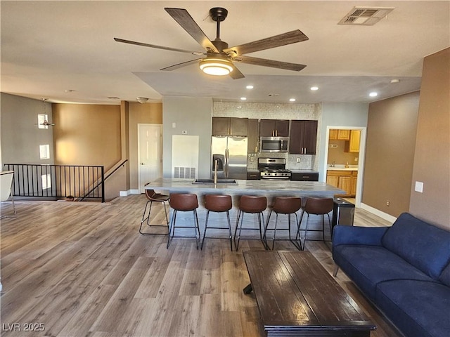 kitchen featuring a kitchen bar, sink, dark brown cabinets, stainless steel appliances, and light hardwood / wood-style floors