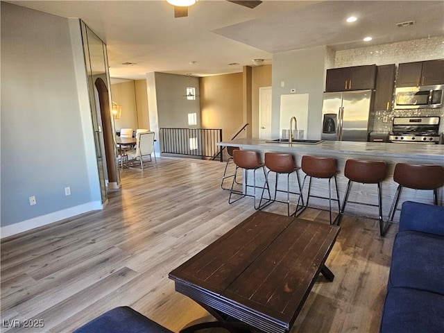 kitchen with sink, light hardwood / wood-style flooring, a breakfast bar area, appliances with stainless steel finishes, and dark brown cabinets