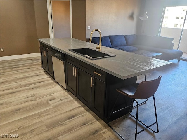 kitchen with sink, a breakfast bar, an island with sink, stainless steel dishwasher, and light wood-type flooring