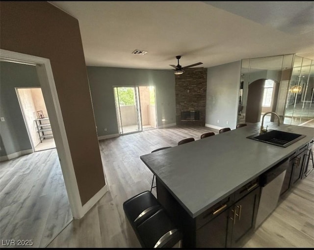 kitchen featuring baseboards, ceiling fan, a sink, arched walkways, and a fireplace