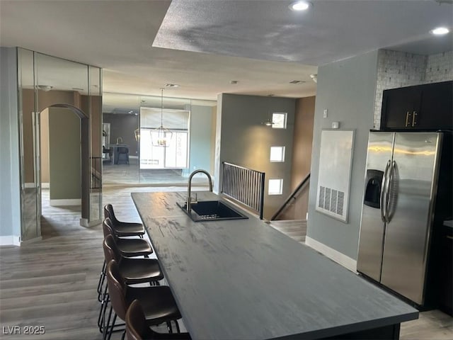 kitchen with a sink, stainless steel fridge, baseboards, and an island with sink