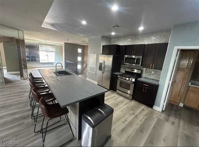 kitchen with light wood-type flooring, stainless steel appliances, dark cabinetry, and a breakfast bar