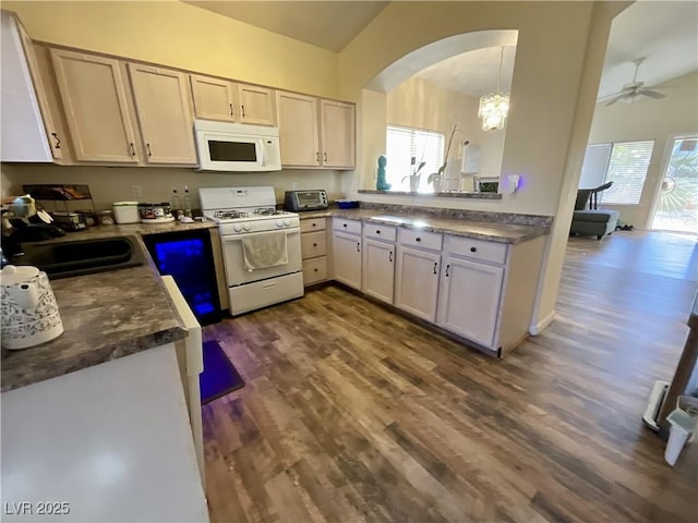 kitchen with ceiling fan with notable chandelier, sink, hanging light fixtures, dark wood-type flooring, and white appliances