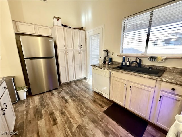 kitchen featuring dark hardwood / wood-style floors, sink, dark stone countertops, stainless steel fridge, and white dishwasher